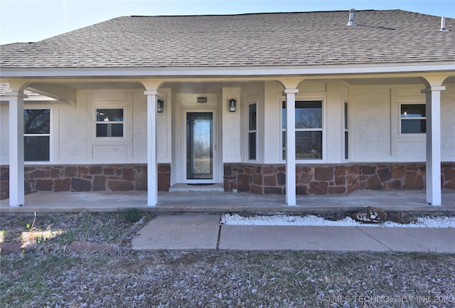 entrance to property featuring covered porch, stone siding, and a shingled roof