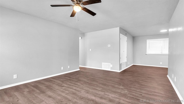 empty room with dark wood-type flooring, a ceiling fan, visible vents, and baseboards