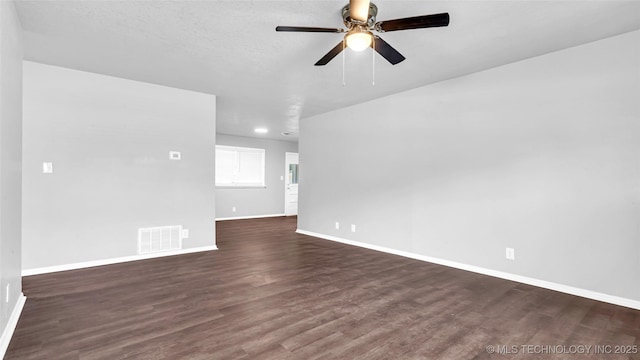 spare room with a ceiling fan, dark wood-style flooring, visible vents, and baseboards