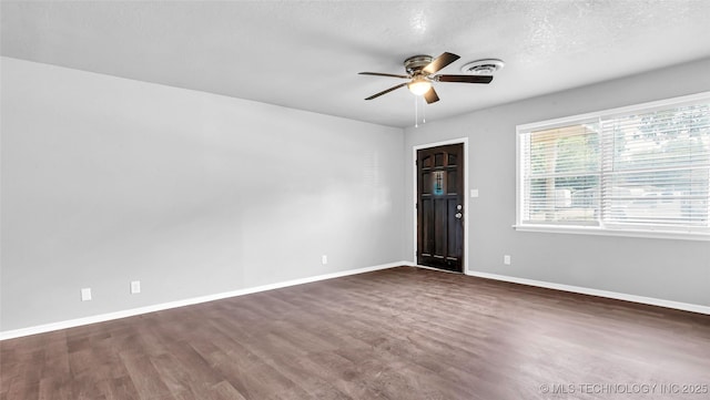 spare room with dark wood-style floors, ceiling fan, visible vents, and baseboards