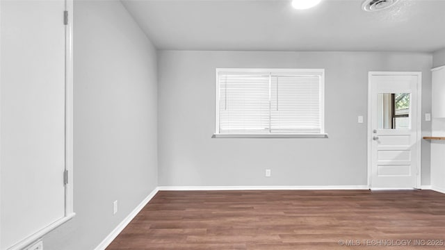 empty room with wood finished floors, visible vents, and baseboards