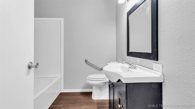 bathroom featuring toilet, a bathing tub, vanity, wood finished floors, and baseboards