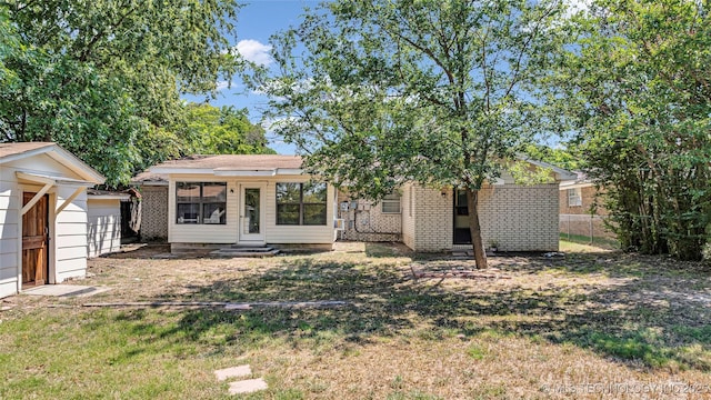 rear view of property with entry steps, brick siding, a lawn, and fence