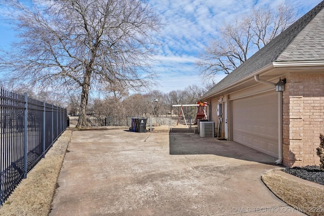 view of yard featuring a garage, concrete driveway, central AC, and fence