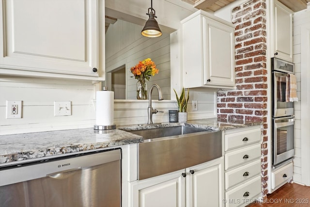 kitchen featuring light stone counters, decorative light fixtures, stainless steel appliances, white cabinets, and a sink