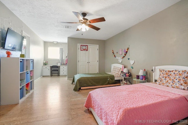 bedroom featuring light wood finished floors, visible vents, ceiling fan, a textured ceiling, and a closet