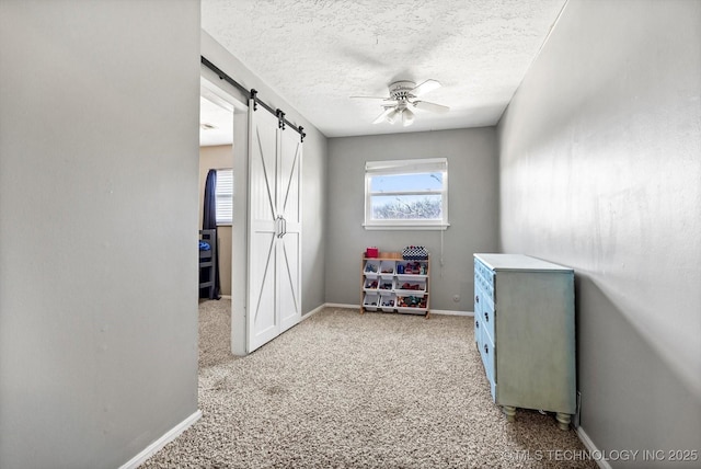 playroom with a textured ceiling, carpet floors, a barn door, and baseboards