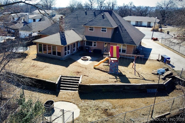 back of property with a fenced backyard, dirt driveway, a playground, and brick siding