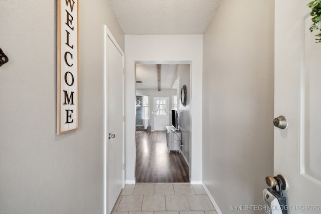 hallway featuring a textured ceiling, light tile patterned flooring, and baseboards