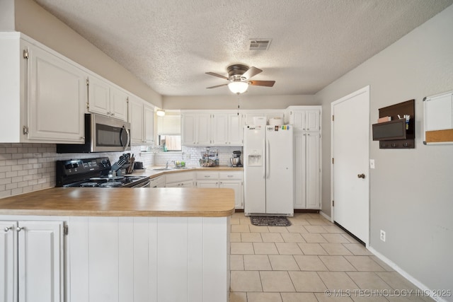 kitchen featuring white refrigerator with ice dispenser, visible vents, stainless steel microwave, black electric range oven, and a peninsula