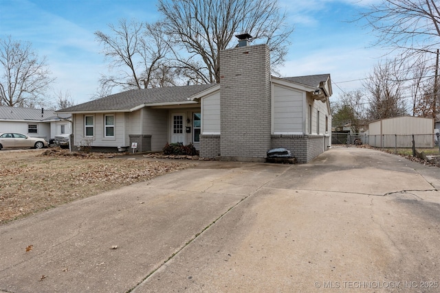 exterior space with concrete driveway, brick siding, a chimney, and fence