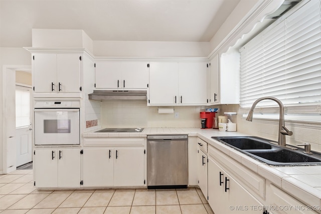 kitchen featuring white oven, tile counters, a sink, dishwasher, and under cabinet range hood