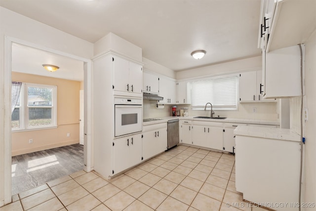 kitchen featuring electric stovetop, light countertops, a sink, oven, and under cabinet range hood