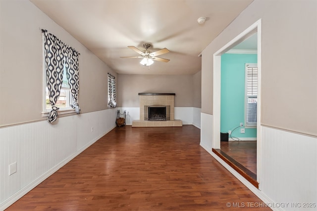 unfurnished living room with ceiling fan, a fireplace, wood finished floors, and wainscoting