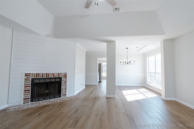 unfurnished living room with crown molding, a fireplace, visible vents, wood finished floors, and ceiling fan with notable chandelier