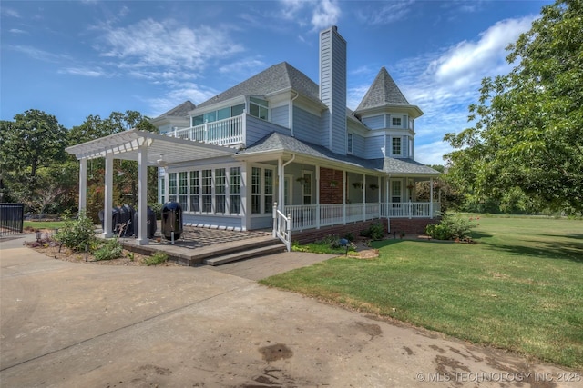 back of property featuring brick siding, a yard, a chimney, a porch, and a pergola