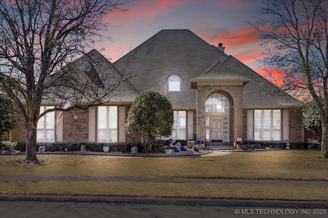 view of front of property with roof with shingles, a chimney, a front lawn, and brick siding