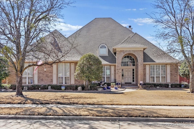 french country style house featuring a shingled roof, a chimney, and brick siding