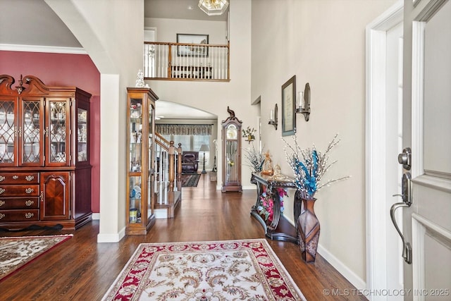 entryway with dark wood-type flooring, arched walkways, baseboards, and stairs