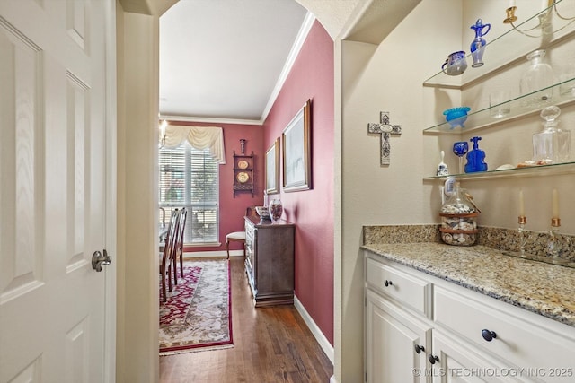 bar featuring baseboards, arched walkways, dark wood-type flooring, and ornamental molding