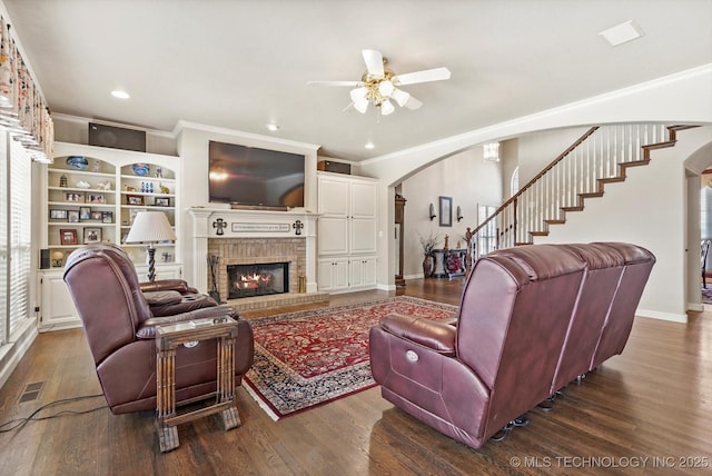 living area with arched walkways, dark wood-style flooring, visible vents, ornamental molding, and a brick fireplace