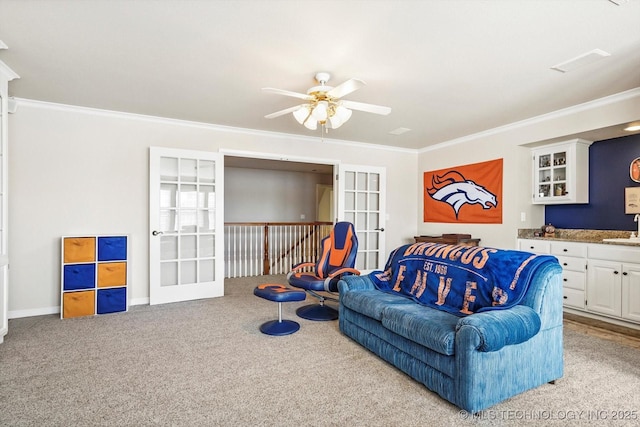 carpeted living room with ceiling fan, a sink, baseboards, ornamental molding, and french doors