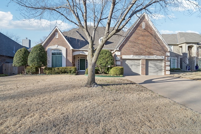 view of front facade with roof with shingles, brick siding, an attached garage, fence, and driveway