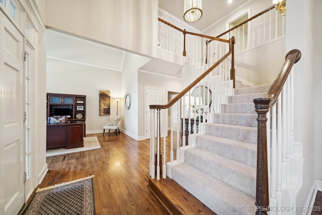 foyer with a towering ceiling, an inviting chandelier, ornamental molding, wood finished floors, and baseboards