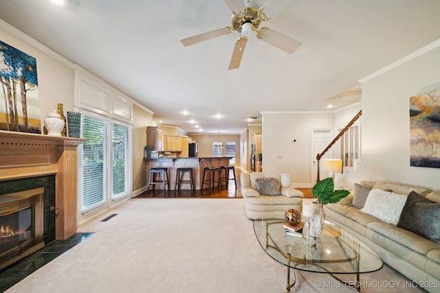 living area featuring visible vents, baseboards, a fireplace with flush hearth, stairway, and ornamental molding