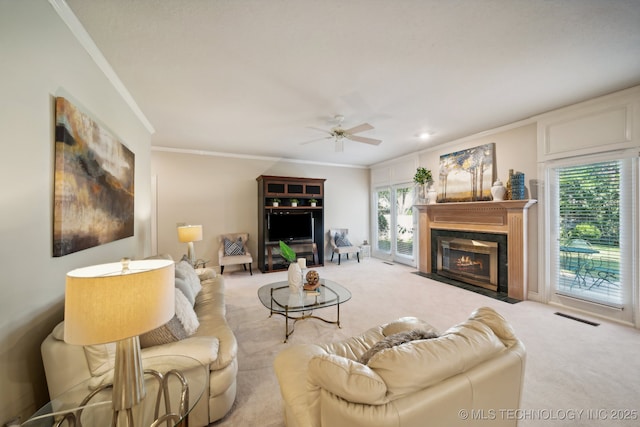 carpeted living room featuring ceiling fan, a fireplace with flush hearth, visible vents, and crown molding