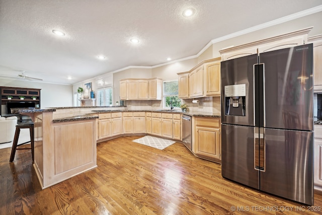 kitchen featuring light wood finished floors, light brown cabinetry, appliances with stainless steel finishes, and a breakfast bar area