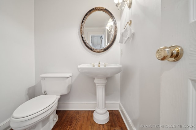 half bathroom featuring wood finished floors, toilet, and baseboards