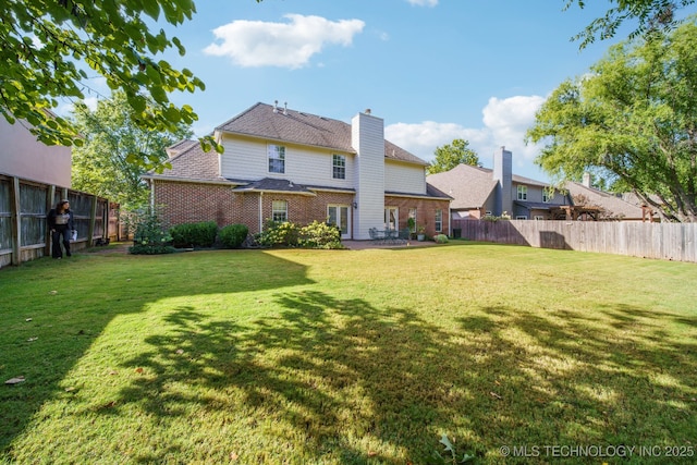 back of house featuring brick siding, a lawn, a chimney, and a fenced backyard