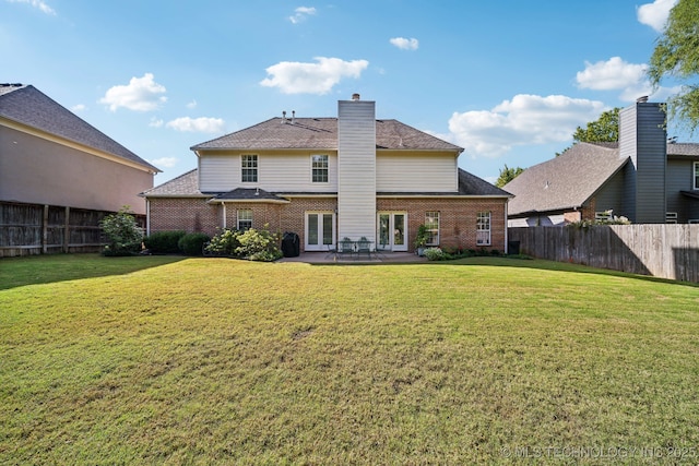 rear view of house with french doors, brick siding, a lawn, and a fenced backyard