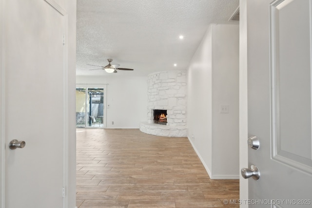 unfurnished living room featuring a textured ceiling, a stone fireplace, light wood-style flooring, visible vents, and a ceiling fan