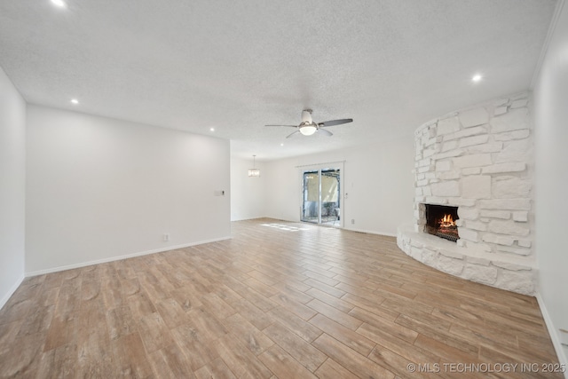 unfurnished living room featuring light wood finished floors, a ceiling fan, a stone fireplace, a textured ceiling, and baseboards