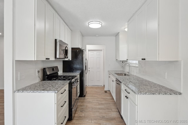 kitchen with appliances with stainless steel finishes, a sink, light wood-style flooring, and white cabinets