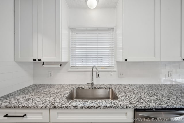 kitchen with dishwasher, tasteful backsplash, a sink, and white cabinetry