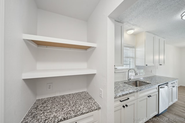 kitchen with open shelves, decorative backsplash, stainless steel dishwasher, light wood-style floors, and a sink