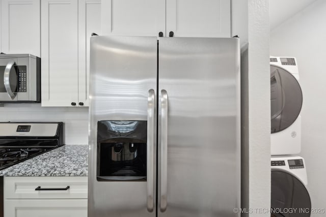 kitchen featuring light stone counters, decorative backsplash, appliances with stainless steel finishes, stacked washer / dryer, and white cabinetry