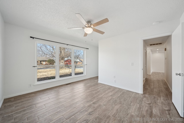 empty room featuring a textured ceiling, ceiling fan, wood finished floors, visible vents, and baseboards