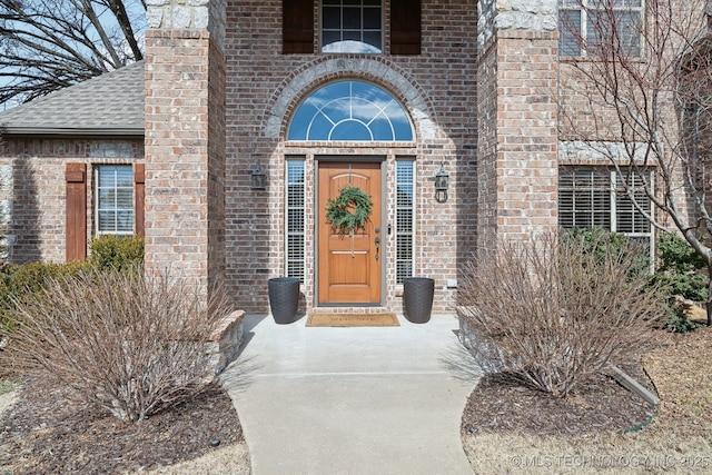 doorway to property with brick siding and roof with shingles