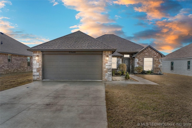 view of front of property featuring roof with shingles, a lawn, a garage, stone siding, and driveway