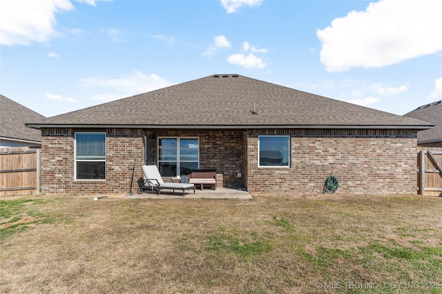 back of house with roof with shingles, a yard, brick siding, a patio, and fence