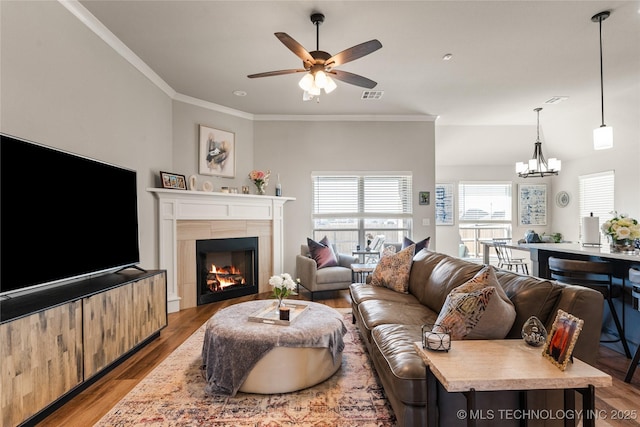 living area with visible vents, ornamental molding, wood finished floors, a fireplace, and ceiling fan with notable chandelier