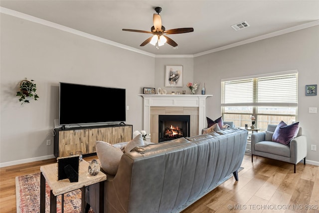 living room featuring a lit fireplace, visible vents, light wood-style flooring, and ornamental molding