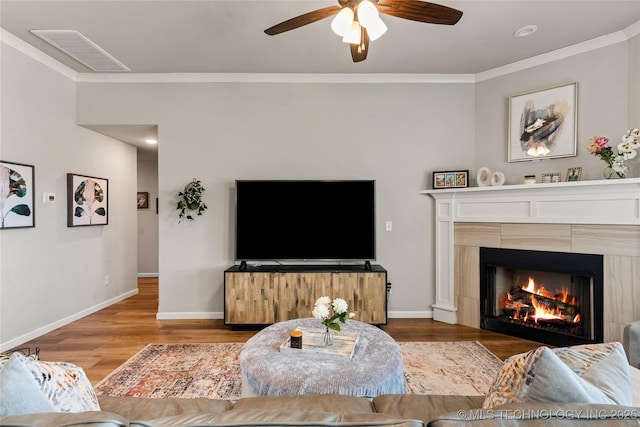 living room featuring a fireplace, visible vents, ornamental molding, wood finished floors, and baseboards