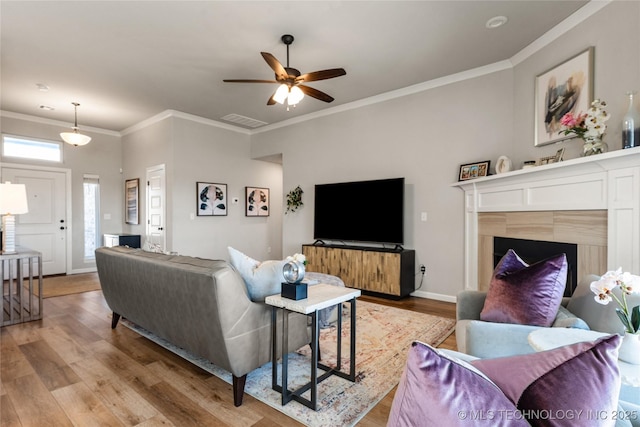 living room featuring ceiling fan, light wood-style flooring, visible vents, baseboards, and ornamental molding