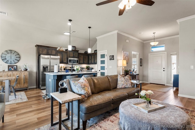 living area with ornamental molding, light wood finished floors, a towering ceiling, and baseboards