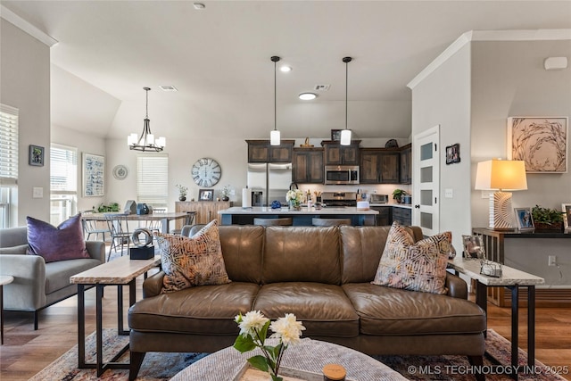 living room featuring a notable chandelier, vaulted ceiling, visible vents, and wood finished floors